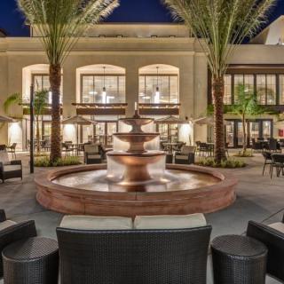A modern outdoor courtyard with a central fountain surrounded by seating, illuminated at night.