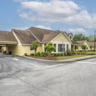 A single-story residential building with a landscaped front and a driveway, under a partly cloudy sky.