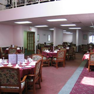 A spacious dining area with neatly arranged tables and chairs, featuring a warm carpeted floor and soft lighting.