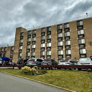 A view of a hotel building with vehicles parked in front under a cloudy sky.
