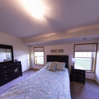 A cozy bedroom with a neatly made bed, a dresser, and two large windows.