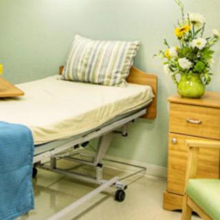 A hospital room with a neatly made bed beside a nightstand with a flower arrangement.