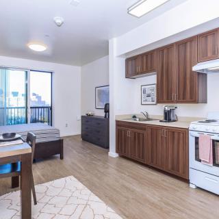 A modern open-space apartment featuring a kitchen with wooden cabinets and a cozy living area with ample natural light.
