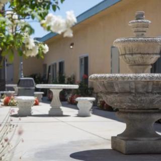 A serene courtyard with a stone fountain, surrounded by patio furniture and flowering plants under a clear blue sky.