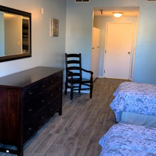 A neatly arranged bedroom featuring twin beds, a dresser with a mirror, and a wooden chair on a wooden floor.