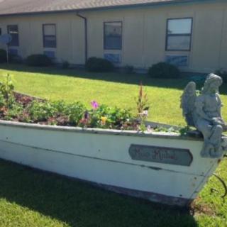 A boat repurposed as a flower bed, featuring an angel statue on the lawn.