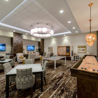 A modern game room with shuffleboard, stylish chandeliers, and comfortable seating.