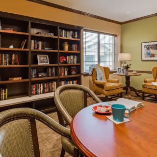 A cozy reading room with a large bookshelf, comfortable chairs, and a table with a mug.