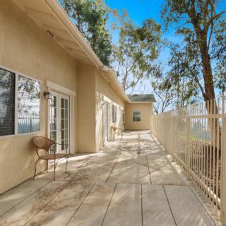 A spacious outdoor patio with a view, featuring a fenced area and surrounded by tall trees.