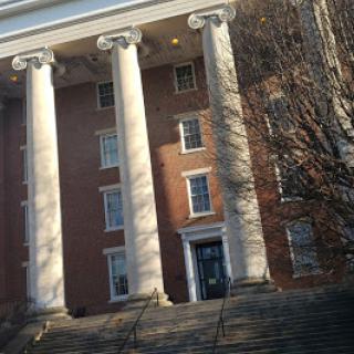 A historic building featuring large columns and a brick facade, complemented by steps leading up to the entrance.
