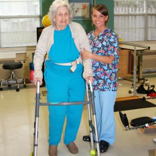 A healthcare worker assists an elderly patient with a walker during a physical therapy session.