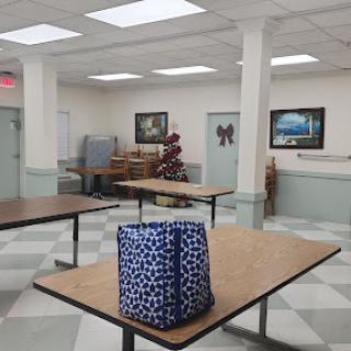 A spacious indoor room with tables, artwork on the walls, and a small tree in the corner.