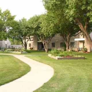 A scenic view of an apartment complex with lush green lawns and trees lining a curved sidewalk.