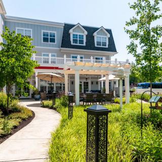 An inviting residential building with a landscaped garden and outdoor seating area under a pergola.