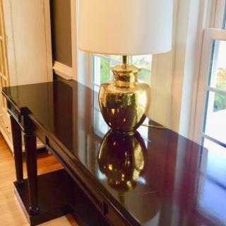 A stylish gold lamp on a glossy wooden table next to a window.