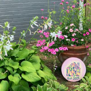 A vibrant garden scene featuring lush hostas and pink flowers in a terracotta planter against a brick wall.