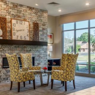 A cozy living room setting with patterned chairs and a table near a fireplace and large windows.