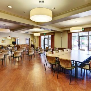 A spacious dining area with multiple tables and chairs, featuring a wooden floor and large ceiling lights.