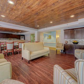 A cozy lounge with wooden ceilings and comfortable seating, including armchairs and a sofa, next to a dining area.