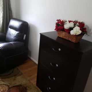 A cozy living room corner with a black dresser, an armchair, and a floral arrangement.