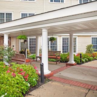 A covered entrance of a building with white columns, surrounded by flowers and benches.