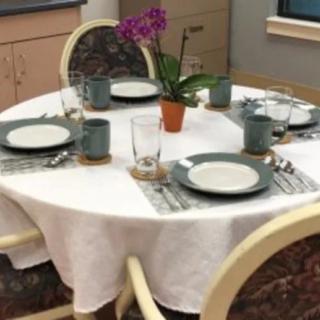 A neatly set dining table with plates, cups, and a potted orchid centerpiece.