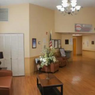 A spacious lobby with comfortable seating, an American flag, and decorative flowers under a chandelier.
