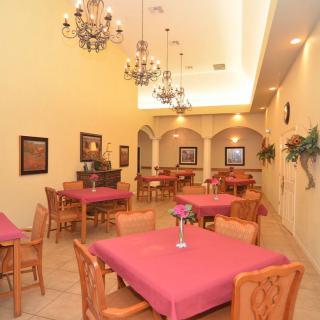An elegant dining room with chandeliers, decorated with pink tablecloths and wooden furniture.