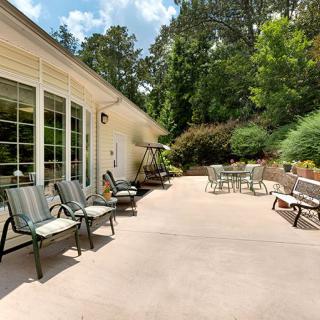 A spacious backyard patio with various seating options, surrounded by lush greenery on a sunny day.