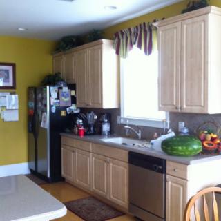 A modern kitchen with wooden cabinets, a refrigerator, and a countertop featuring a watermelon and fruit basket.