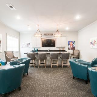 A modern lounge area featuring armchairs, bar stools, and a large television.