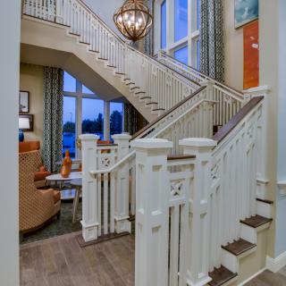 A modern living room featuring a stylish staircase with white railings, large windows, and an elegant chandelier.