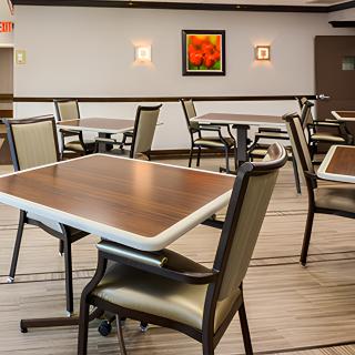 An empty dining area with neatly arranged tables and chairs, featuring artwork on the wall.