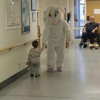 A child in a hospital hallway interacts with a person in a bunny costume.