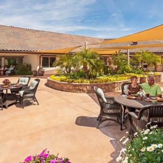 People enjoying a sunny day on a spacious outdoor patio with tables and chairs surrounded by vibrant flowers.