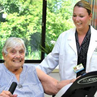 An elderly woman engaging in a fitness activity with the support of a healthcare professional.