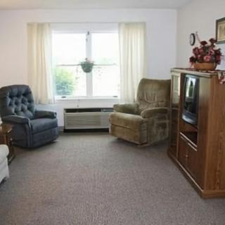 A cozy living room with armchairs, a television, and a large window with curtains.