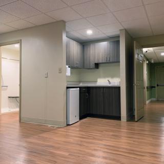 A basement with a small kitchenette, featuring wood flooring and modern cabinets.