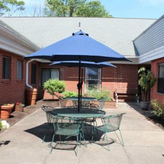A sunny courtyard with a blue umbrella over outdoor furniture, surrounded by brick buildings.