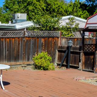 A sunny backyard with a wooden deck and gazebo, surrounded by a fence and trees.