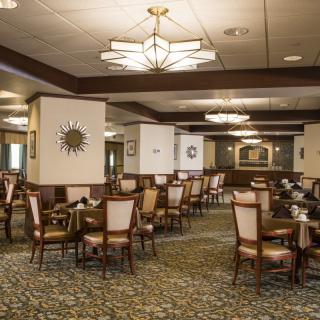 An elegant dining room with neatly arranged tables and chairs, featuring stylish lighting and a carpeted floor.