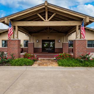 A brick building entrance adorned with American flags and surrounded by neat landscaping.