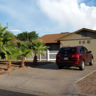 A suburban house with a car parked in the driveway, surrounded by palm trees.