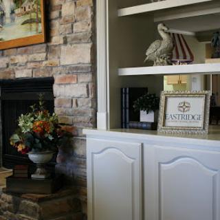 A cozy living room corner with a stone fireplace, decorative flowers, and an inviting shelf.