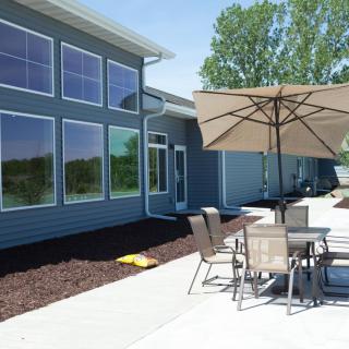 A modern patio setup with furniture and an umbrella outside a house with large windows.
