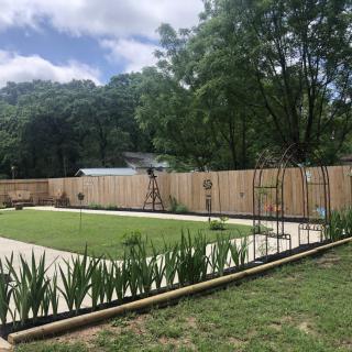 A neatly landscaped garden with a central lawn, bordered by a wooden fence and surrounded by trees.