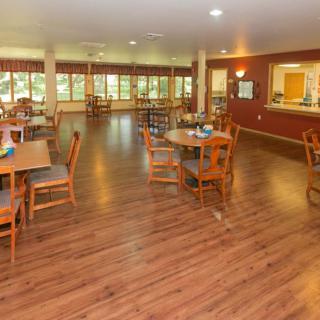 A spacious dining area with wooden floors, several tables and chairs, and large windows providing natural light.