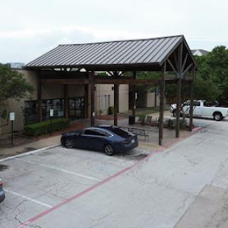 A modern building with a metal roof and a covered entryway, surrounded by a parking lot.
