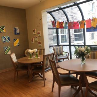 A cozy dining area adorned with colorful artwork and fresh flowers, featuring round tables and large windows.