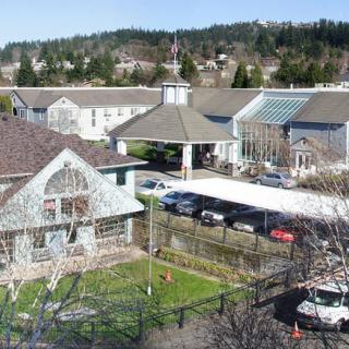 An aerial view of a residential area with several buildings, cars parked, and trees in the background.